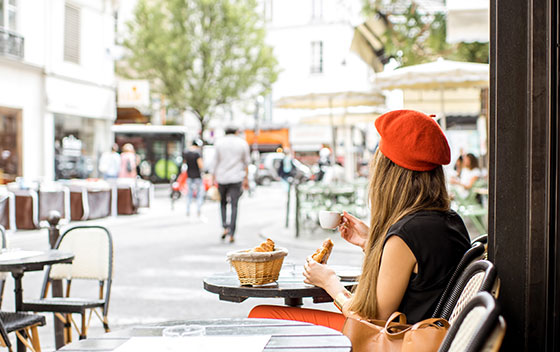 Femme avec béret rouge en terrasse à Paris, prenant un petit-déjeuner avec café et croissant