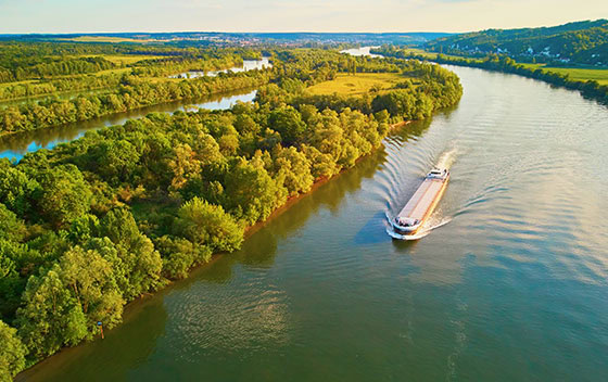 Vue aérienne panoramique sur la Seine où se trouve une péniche, et sur les champs verdoyants de la campagne