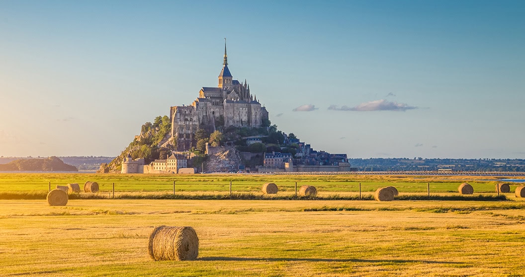 Belle vue sur l'île de marée du Mont Saint-Michel, belle lumière dorée le soir au coucher du soleil en été avec des balles de foin sur les champs vides