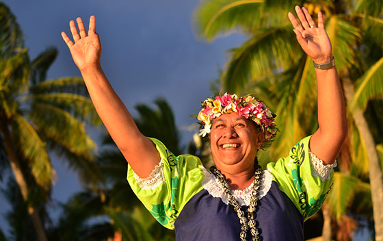 Portrait d'une femme d'île Polynésienne du Pacifique, heureuse et souriante, sur une plage tropicale avec des palmiers à l'arrière-plan.