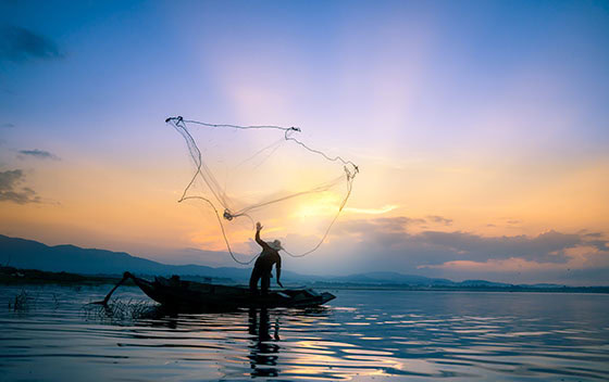 pêcheur asiatique sur bateau en bois pour attraper des poissons d'eau douce dans un réservoir au petit matin avant le lever du soleil